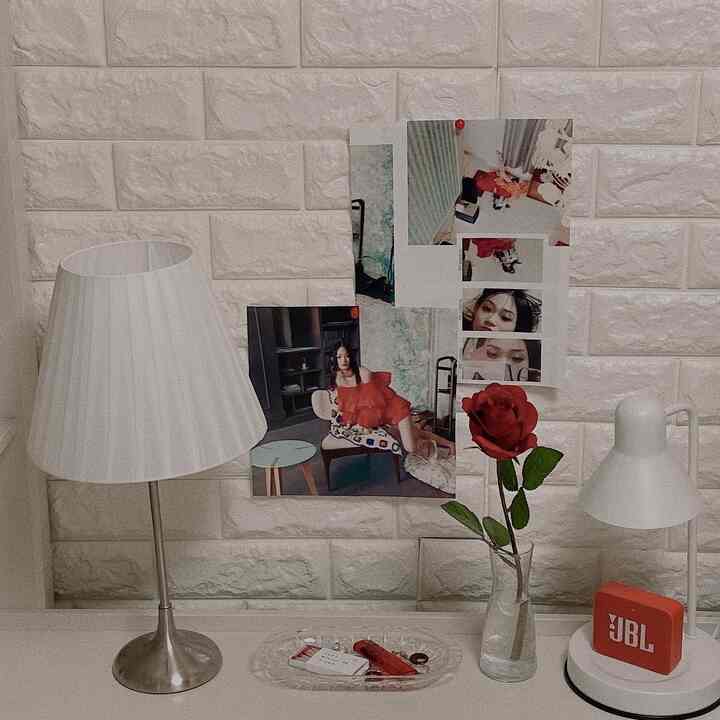 ホワイトブリックの壁を背景に、小さなデスクに2つのテーブルランプと赤いバラの花瓶が配置された、ヴィンテージ感のある空間