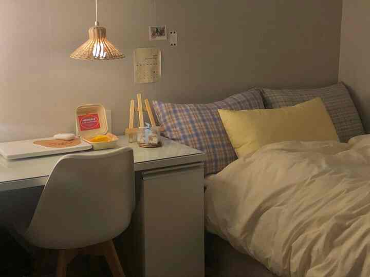 落ち着いたグレーの壁にホワイトの寝具とシンプルなデスクが配置された6畳サイズのワンルーム寝室の雰囲気のあるインテリア