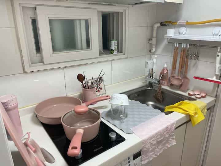 Compact kitchen with pink-tone cookware and utensils arranged neatly around the sink and stovetop