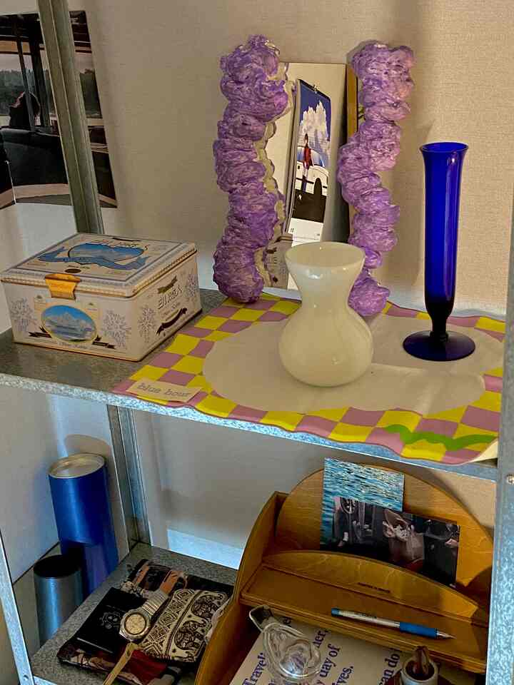 白と青のトーンが印象的なワンルームの棚に、ビンテージの小物と花瓶が配置された雰囲気のあるインテリア