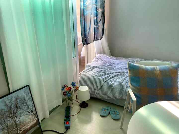 White and green toned studio bedroom featuring bedding, cushions, artwork, and lighting with a natural, minimal atmosphere