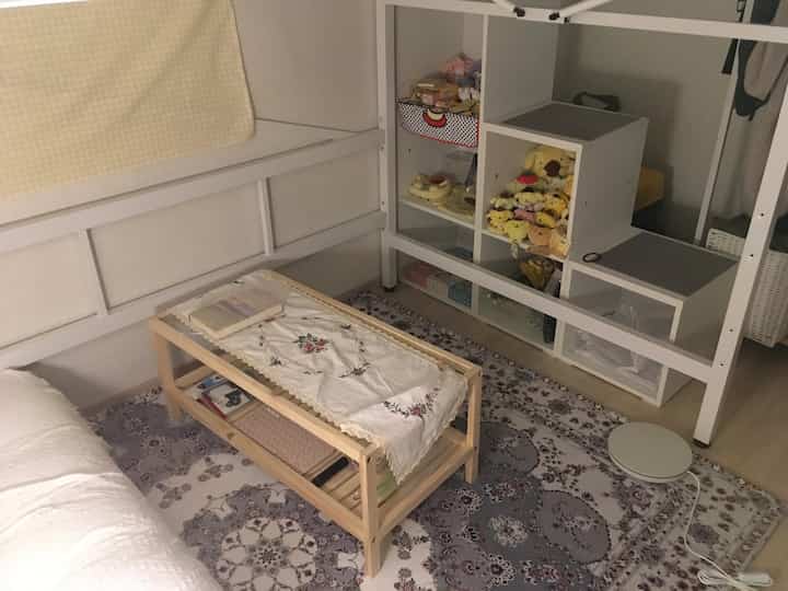 Natural tone studio apartment featuring wooden coffee table and bookshelf with children's toys creating cozy atmosphere