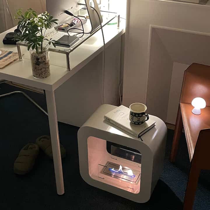 A modern home office space in white tones featuring a mini ethanol fireplace, coffee cup, and mood lamp in a cozy atmosphere