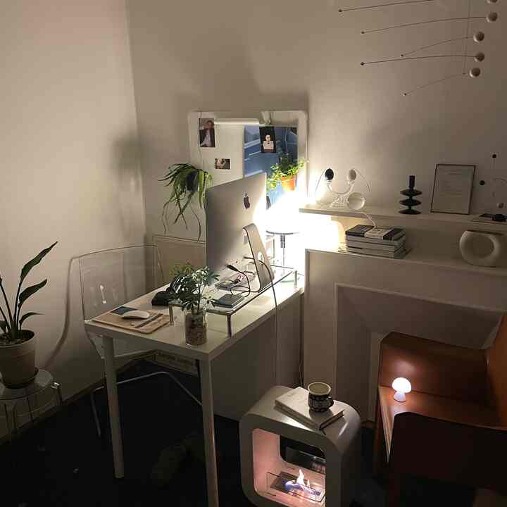 A tranquil natural-tone studio home office with plants and a mobile, featuring a mini stove and mushroom lamp adding cozy ambiance