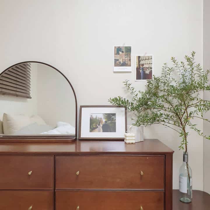 Warm natural wood tone room featuring a wooden dresser topped with a mirror and picture frame in a simple space