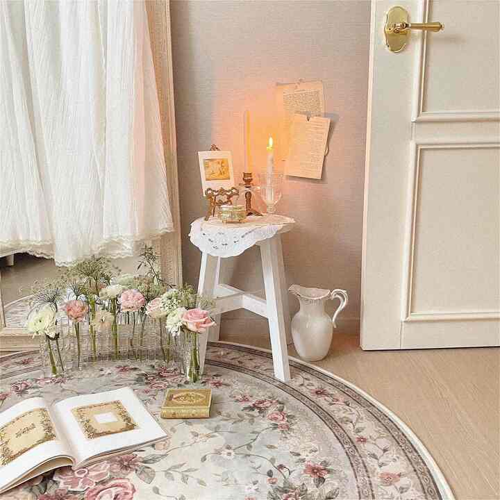 White and beige toned corner space featuring floral carpet, lace-covered stool with candles, and antique decor creating a cozy atmosphere