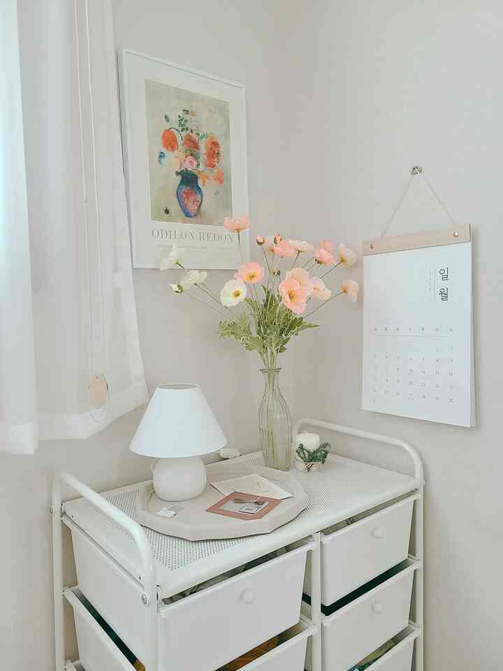 Bright and simple white and beige toned corner storage featuring a vase with flowers and a drawing frame in a warm setting