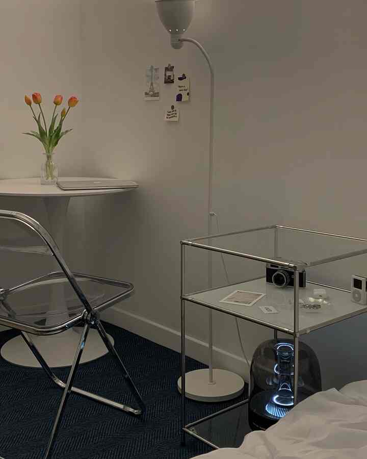 White and blue toned living space featuring transparent chair, floor lamp, and vase with tulips creating a clean, modern atmosphere