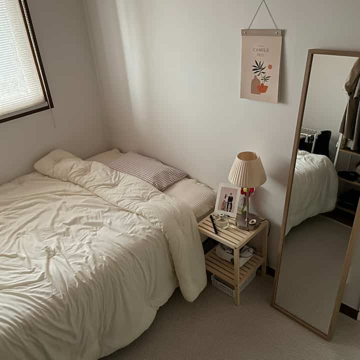 Natural color bedroom featuring bedding, a full-length mirror and nightstand arranged in a cozy setting