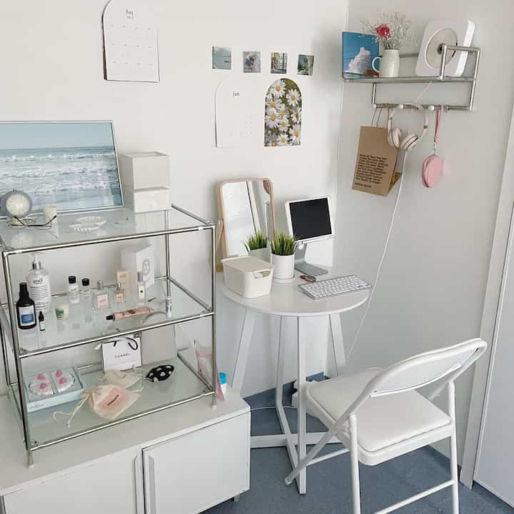White and gray toned small workspace featuring a folding chair, compact desk, organized shelves and a mirror in a modern room