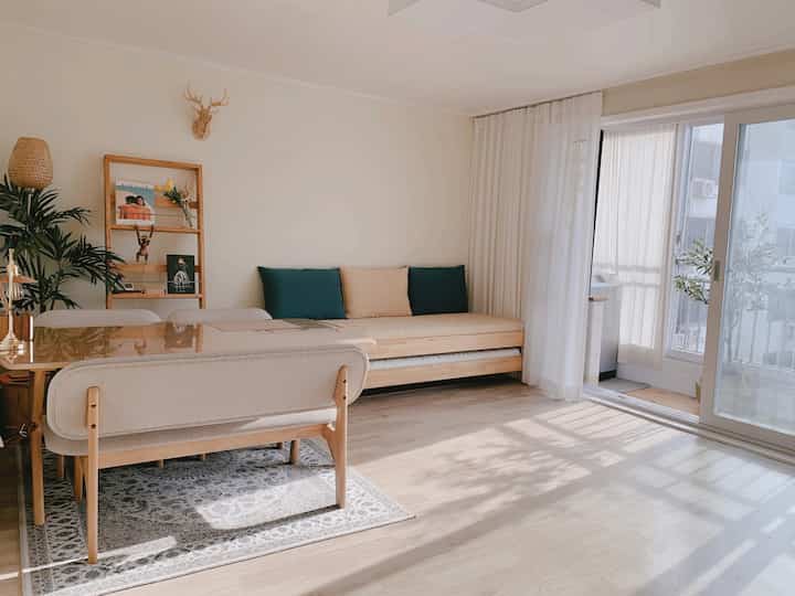 Bright and cozy dining room in natural wood tones with white and beige, featuring large window and sheer curtains illuminating the space