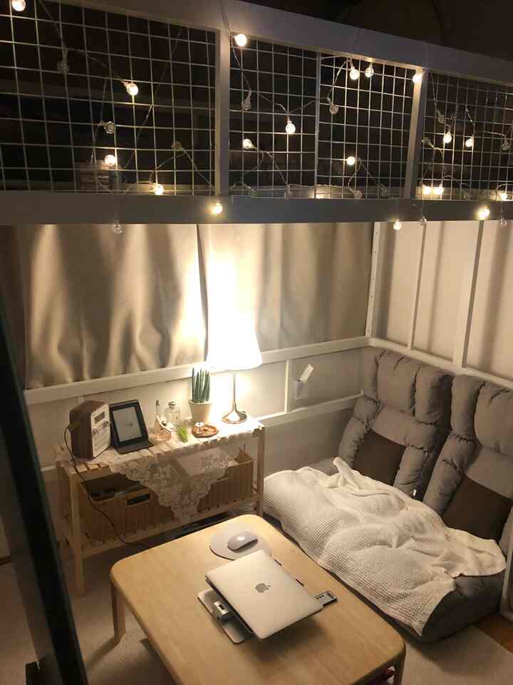 Cozy small bedroom in soft light brown and white tones featuring a comfortable armchair and warm string lights, serving as a home office and relaxation spot