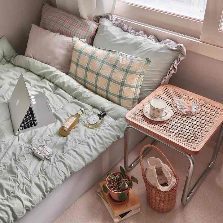 Soft green and natural-toned bedroom featuring rattan stool and side table with cozy bedding creating a warm atmosphere