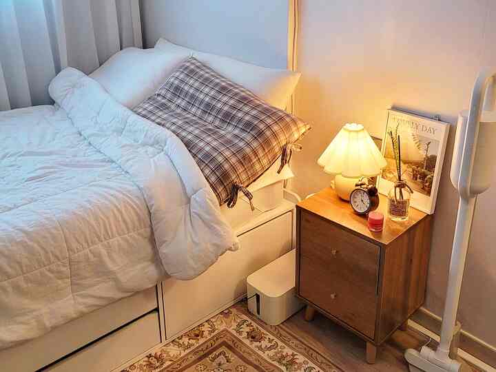 A soft white and warm brown bedroom featuring a cozy bed, wooden nightstand, and a table lamp creating a cozy atmosphere