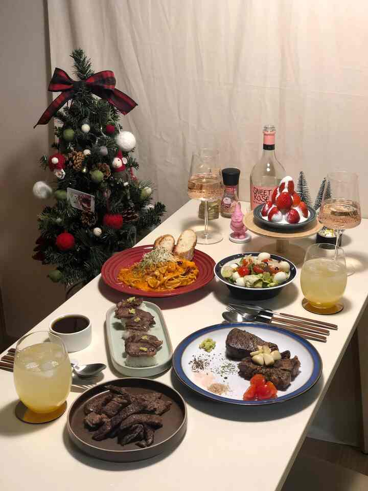 アイボリー色調のキッチンスペース、ダイニングテーブルを中心にクリスマスツリー、多彩な料理とワイングラスが配置された雰囲気のあるホームパーティー