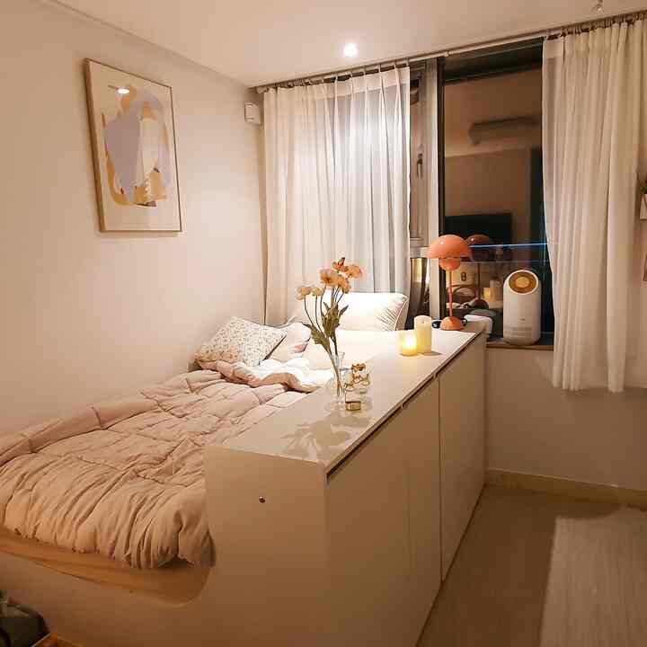 Pale pink bedding and white storage cabinet in a cozy 6-pyeong studio bedroom, warm serene atmosphere
