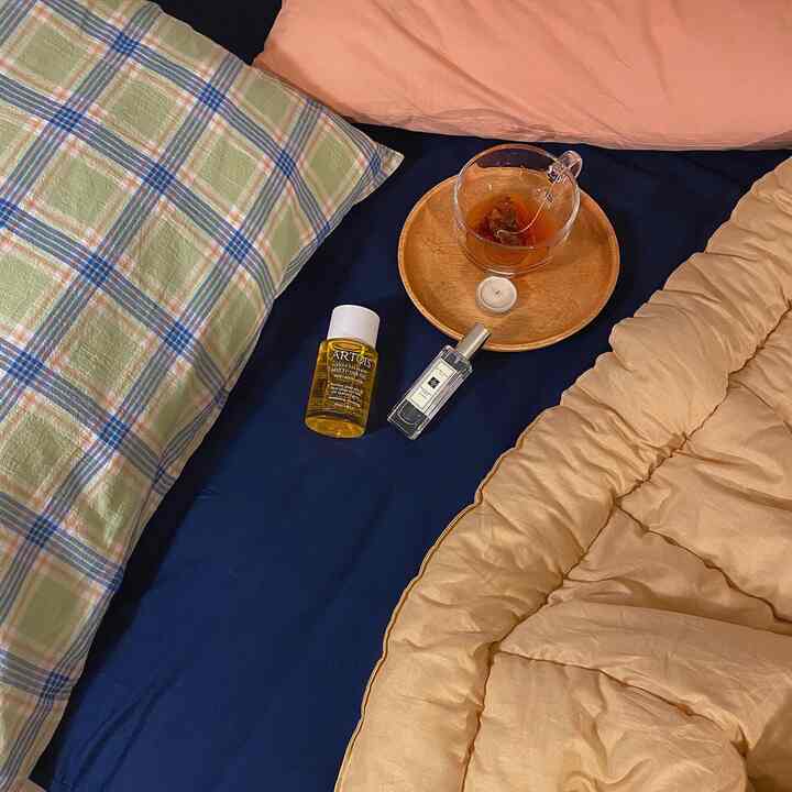 A bedroom scene with navy bed sheet and beige duvet cover, featuring tea and candle creating a cozy home cafe ambiance