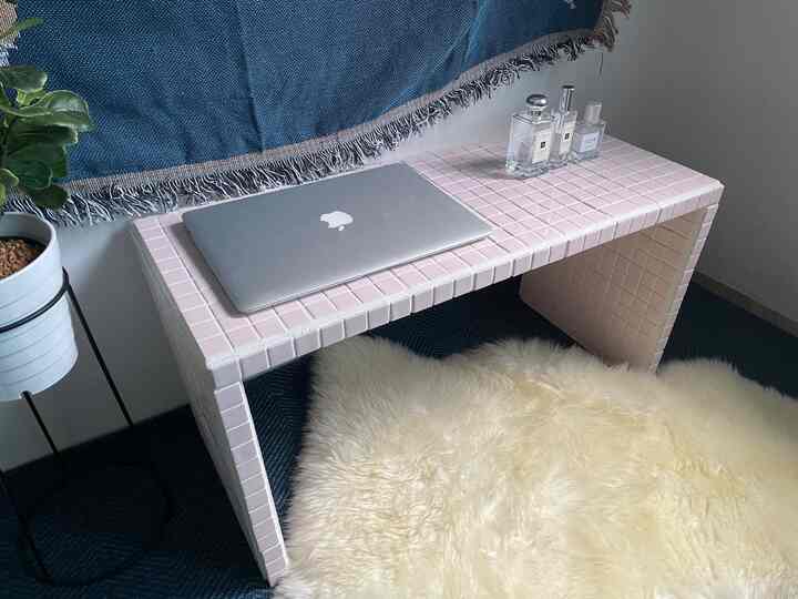 Pastel pink tiled table and cream sheepskin rug in small room, featuring a home office setup and cozy home cafe vibe