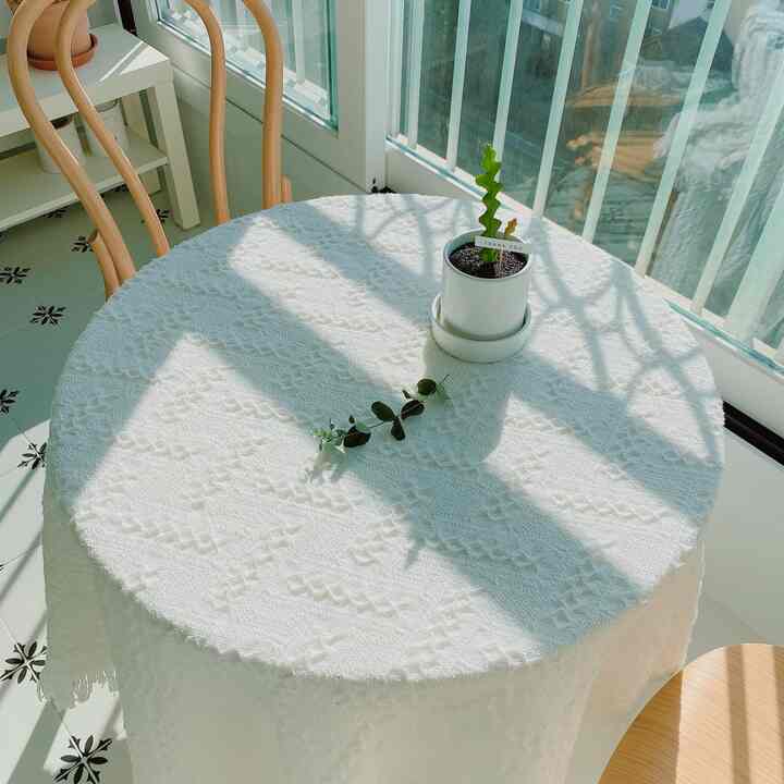 白いテーブルクロスがかかった丸いダイニングテーブルと木製の椅子が配置された、陽光あふれるバルコニーのナチュラルな空間