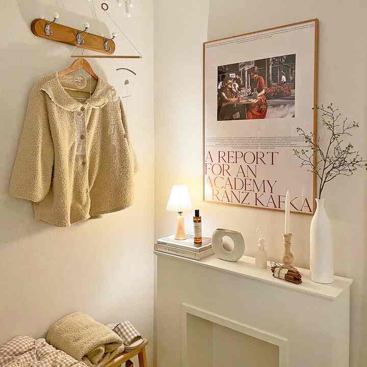 A beige and natural toned living room featuring a fireplace console with a framed poster and various objets, creating a simple atmosphere
