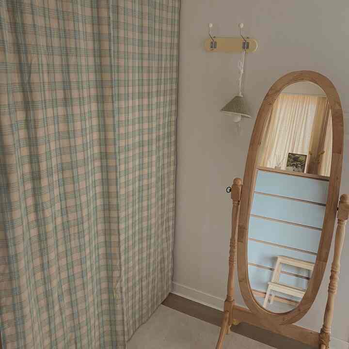 ナチュラルなベージュと淡い木目調のウォークインクローゼット、チェック柄カーテンと全身鏡、木製ステップスツールがある印象的な空間