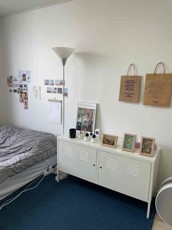 White and blue toned bedroom featuring a white cabinet, posters, and bed, creating a neat and minimalist space