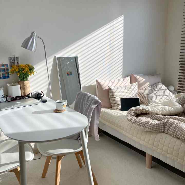 暖かいベージュとホワイトのトーンのワンルーム寝室、ダイニングテーブルとベッドが配置された自然で落ち着いた雰囲気の空間