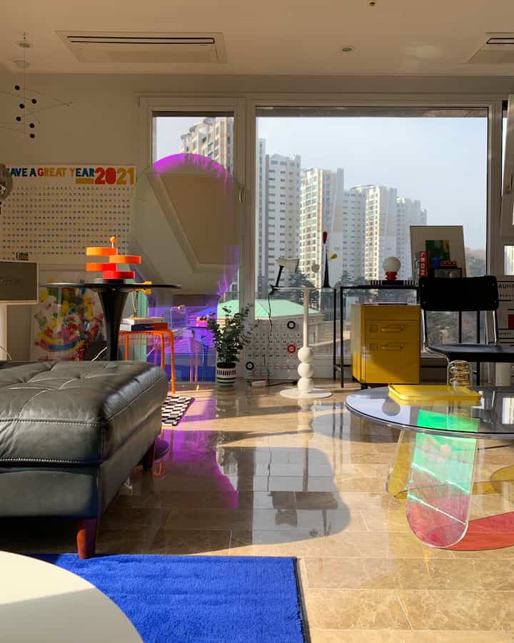 ナチュラルカラーとブルー・イエローのアクセントが調和したリビング、ソファやラグ、個性的なモビールと鏡が配置された印象的な空間