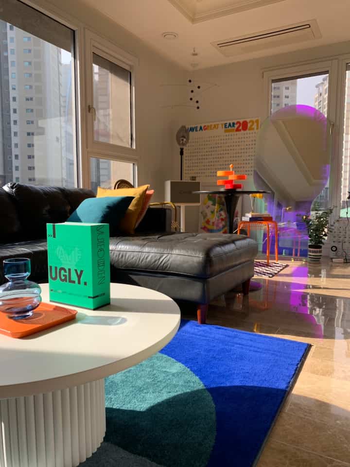 Modern living room featuring a large black leather sofa and blue rug, brightened by ample natural light from tall windows, creating a cozy atmosphere