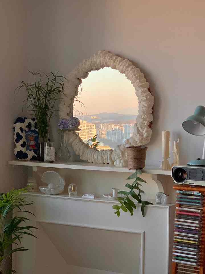 Cozy living space featuring a soft white decorative fireplace and natural green plants with a large, textured mirror