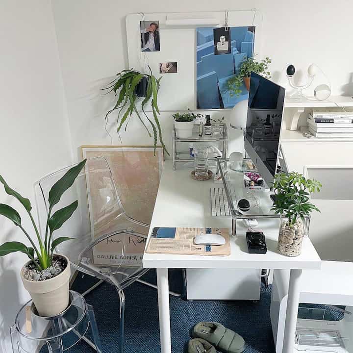 White and transparent materials define a single household home office featuring a computer desk and green plants in a tidy workspace