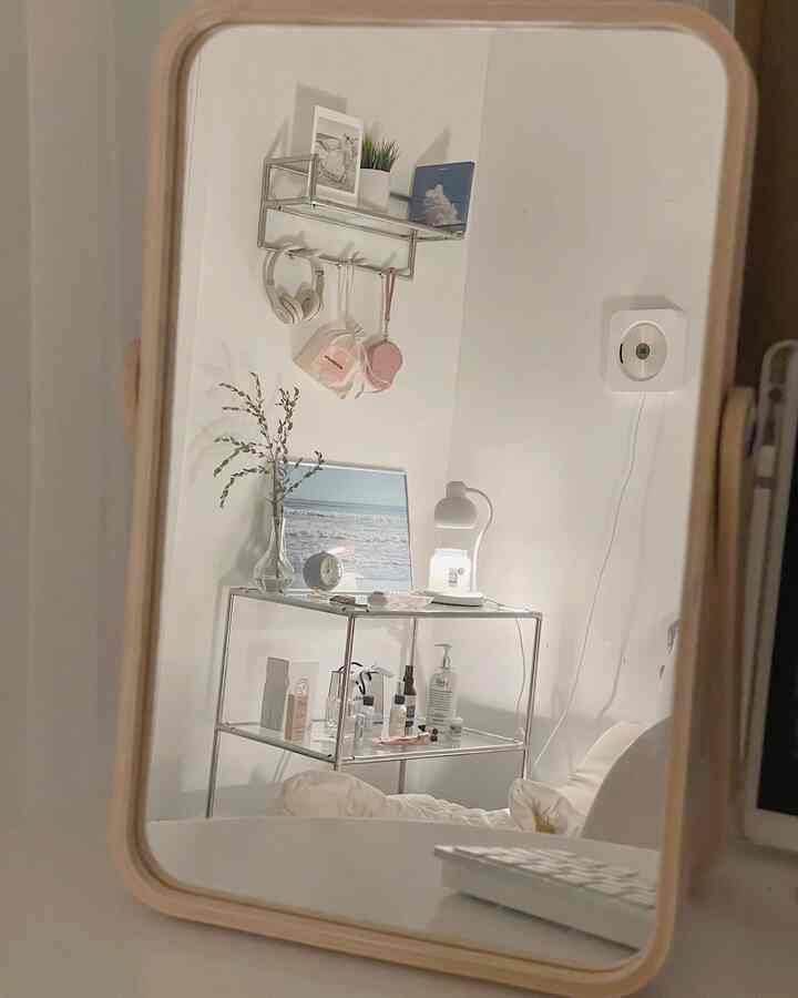 White-toned studio apartment with minimal metal shelves, mirror, and table lamp creating a clean atmosphere