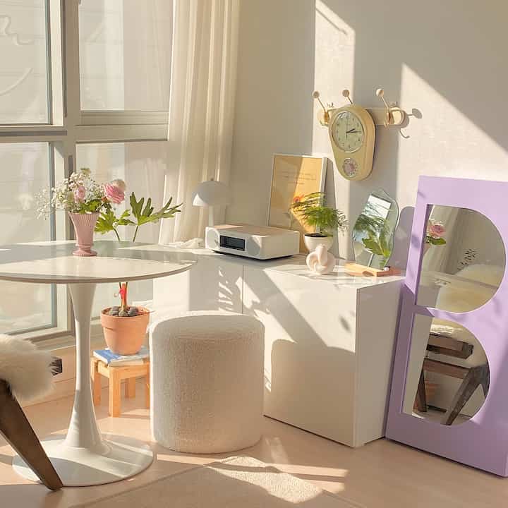 Soft white and light brown toned living room featuring a round table, textured stool, plants, and vase creating a cozy home cafe atmosphere
