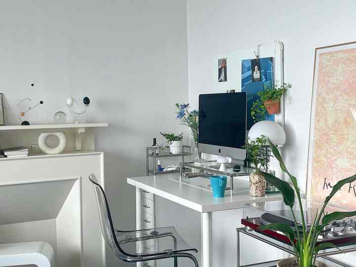 Modern home office in white tones featuring a white desk and transparent chair in a clean workspace