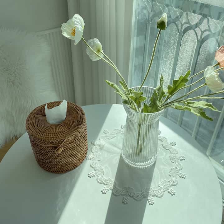 Cozy space with soft white and natural brown tones, featuring a dining table with a vase and lace table runner