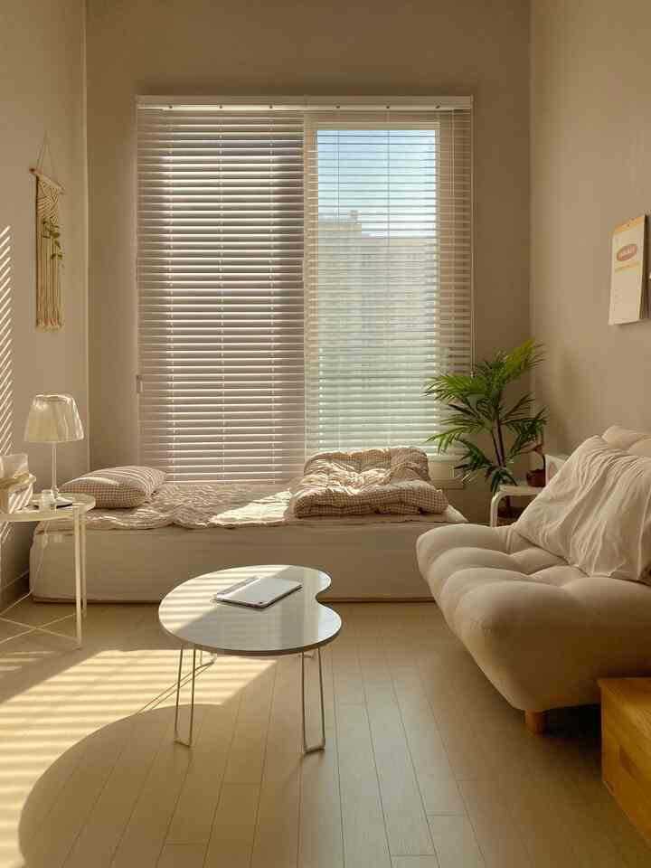 ベージュとホワイトのトーンのワンルーム、ソファとベッド、コーヒーテーブルが配置された雰囲気のあるナチュラルなインテリア