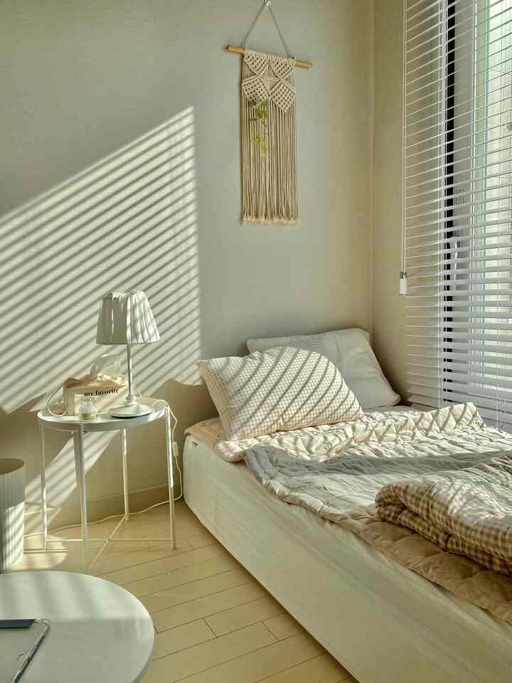 白とベージュのトーンの寝室、ブラインドから差し込む陽光が温かみのある雰囲気を演出するインテリア