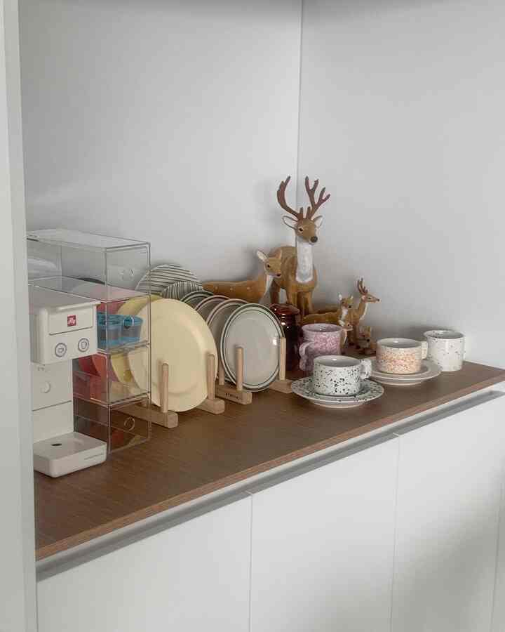 White walls and wood tone countertop featuring a coffee machine, plate rack, and mugs neatly arranged in a clean home cafe space