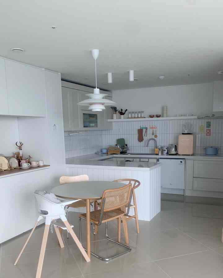 ホワイトとナチュラルウッドトーンが調和したモダンなキッチンとダイニング、赤ちゃん用ハイチェアが配置された清潔感のあるインテリア