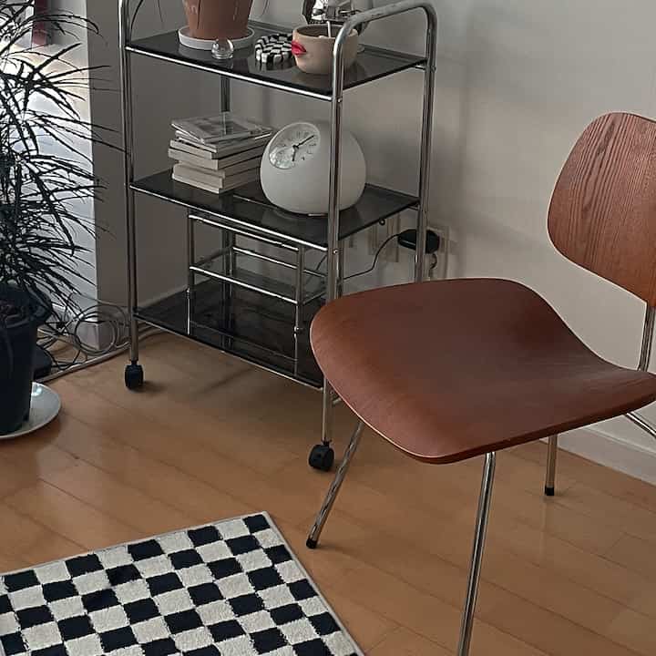 Modern space with white walls and wood-toned chair featuring a metal shelf holding a clock and decorative items