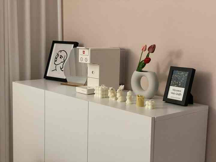 White-toned cabinet topped with Illy coffee machine, candles, vase with flowers, and picture frames in a home cafe setting