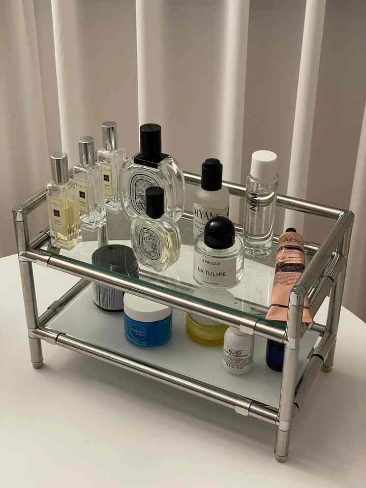 Vanity with silver metal modular storage against white curtain background, neatly arranged perfumes and cosmetics