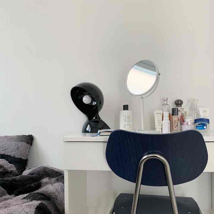 白い壁とネイビーチェアが配置されたシンプルで整った寝室、化粧台と黒いテーブルランプが特徴的なインテリア