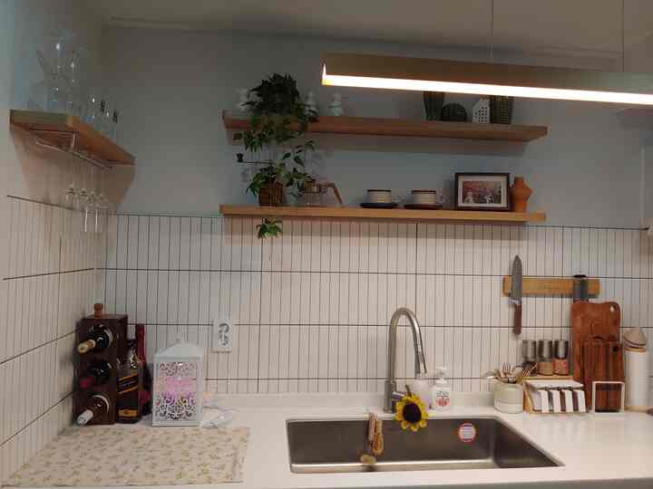 白いタイルと木の棚が調和したキッチン、シンクと植物の装飾が温かみのある雰囲気を演出する空間