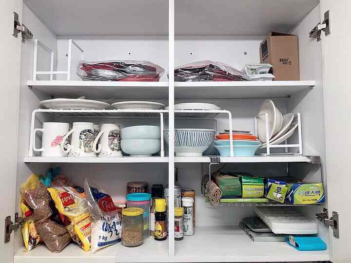 White kitchen cabinet interior with plates and bowls neatly arranged on versatile shelves and organizers, showing organized storage