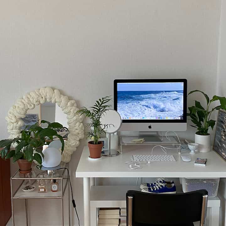 White-toned studio apartment home office featuring a white desk with an iMac and several plants, neat modern interior