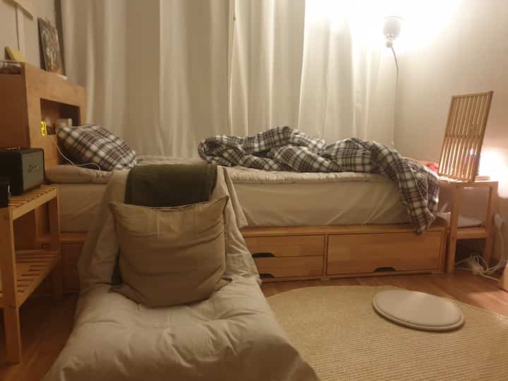 Warm brown and natural toned single bedroom featuring storage bed and cozy cushioned chair in a comfortable atmosphere