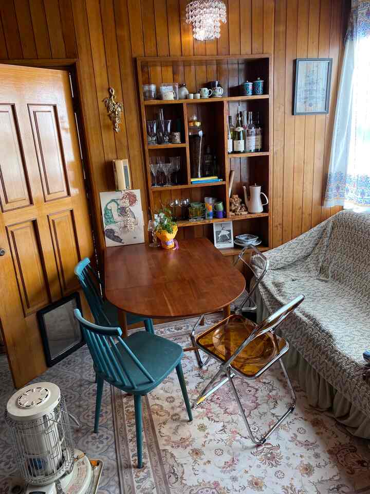 ナチュラルな木目調の壁とレトロな家具が調和したリビングのダイニングスペース、カップや照明が温かみのある雰囲気を演出