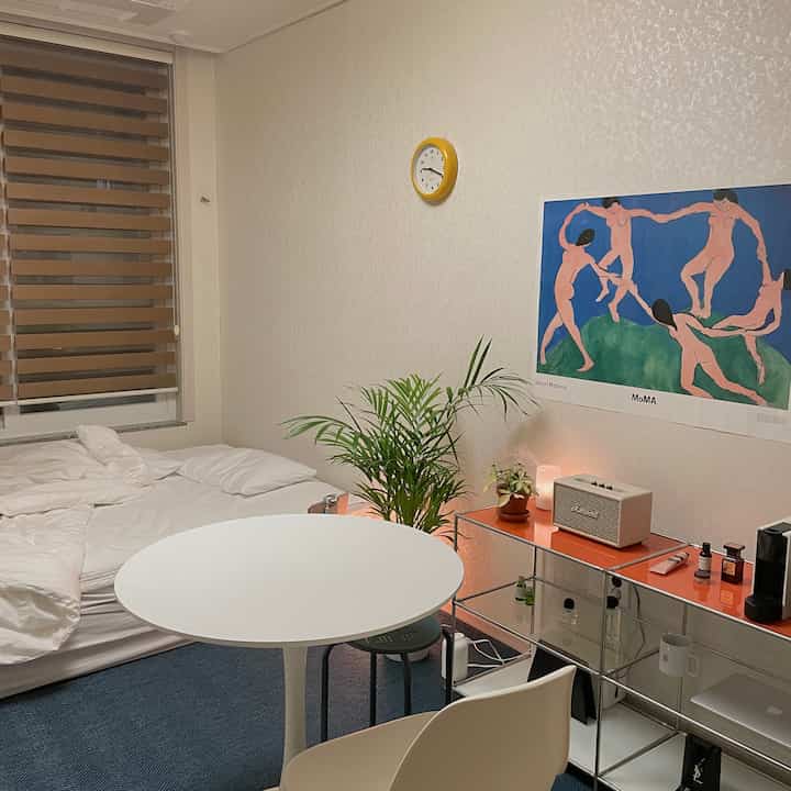 White-toned bedroom featuring a Mid-Century Modern dining table and chairs, with a Matisse poster creating a clean and cozy ambiance