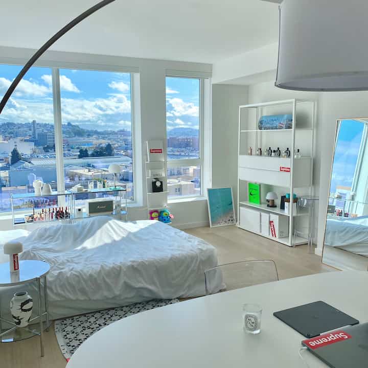 Bright white and natural-tone studio apartment featuring a white bed centrally, IKEA furniture, and clear organized layout